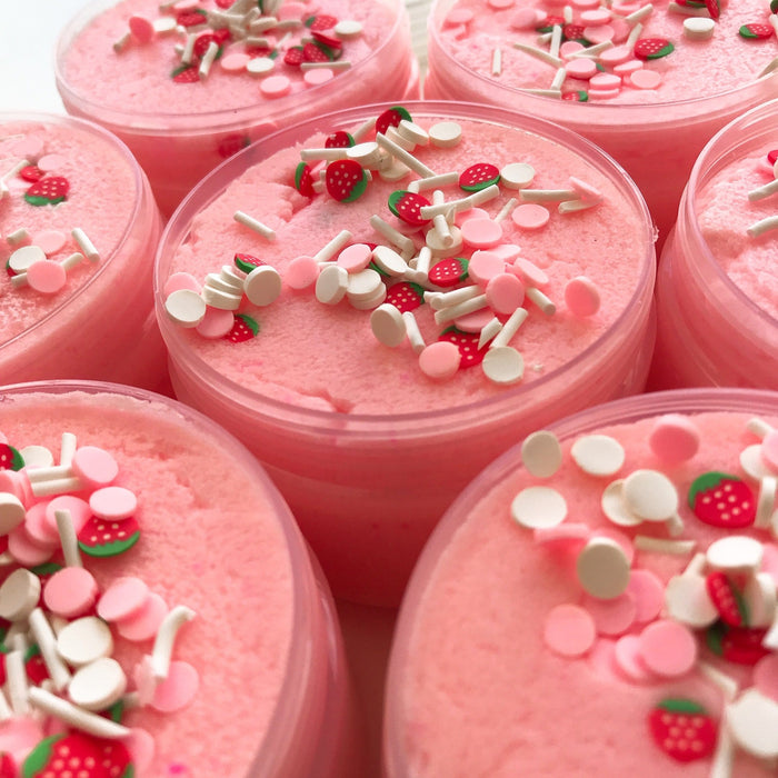 Close up to a pink cloud creme slime in its container with pink and white sprinkles and strawberry sprinkles as decoration