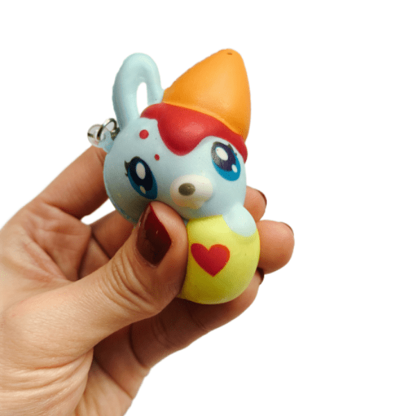 A hand squishing a light blue bunny squishy keychain with an ice cream cone on its head and inside a yellow teacup with a red heart.