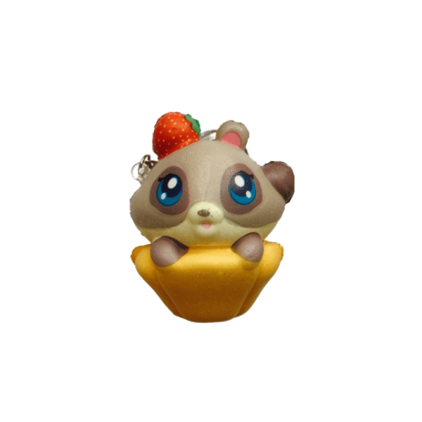 A squishy keychain in the shape of a racoon with a red strawberry on the right side of its head and a cupcake -like base