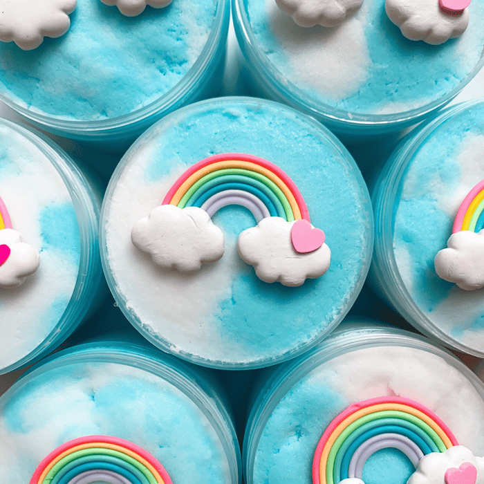 Several white and blue cloud slimes decorated with a charm of a colorful rainbow with two clouds and a small pink heart on the right. 