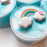 Close up to a white and blue cloud slime decorated with a charm of a colorful rainbow with two clouds and a small pink heart on the right.