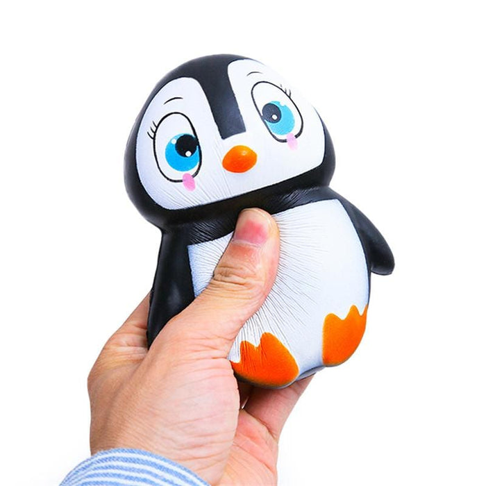 A hand squishing a black penguin squishy with a white belly, orange beak and feet, blue eyes and pink cheeks