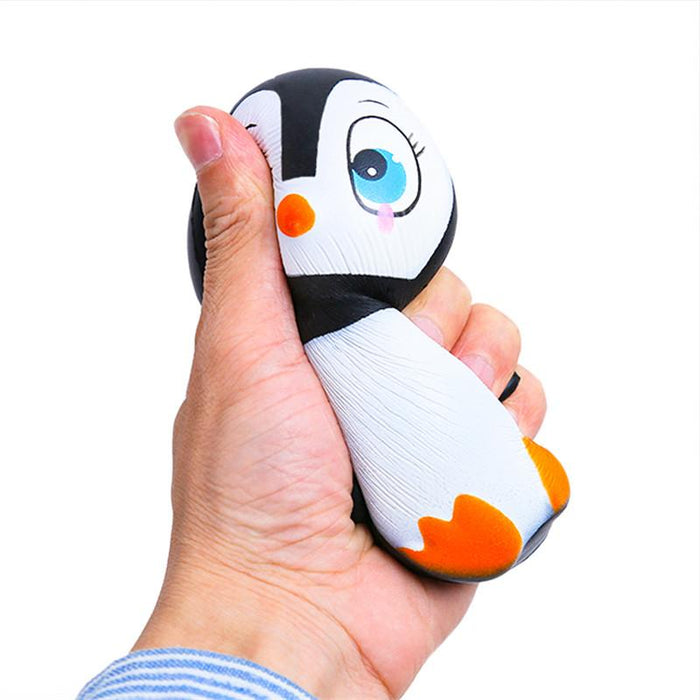 A hand squishing a black and white penguin with blue eyes and orange beak and feet